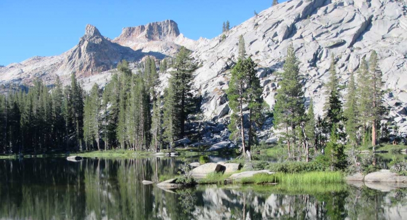 An alpine lake rests among evergreen trees and gray mountains 